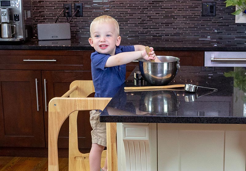 Kid using Montessori furniture standing on a learning toddler tower cooking